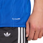 Close-up of a person wearing a blue Adidas Climacool athletic top and black Adidas shorts with white stripes, with the person's hand resting near the shorts.