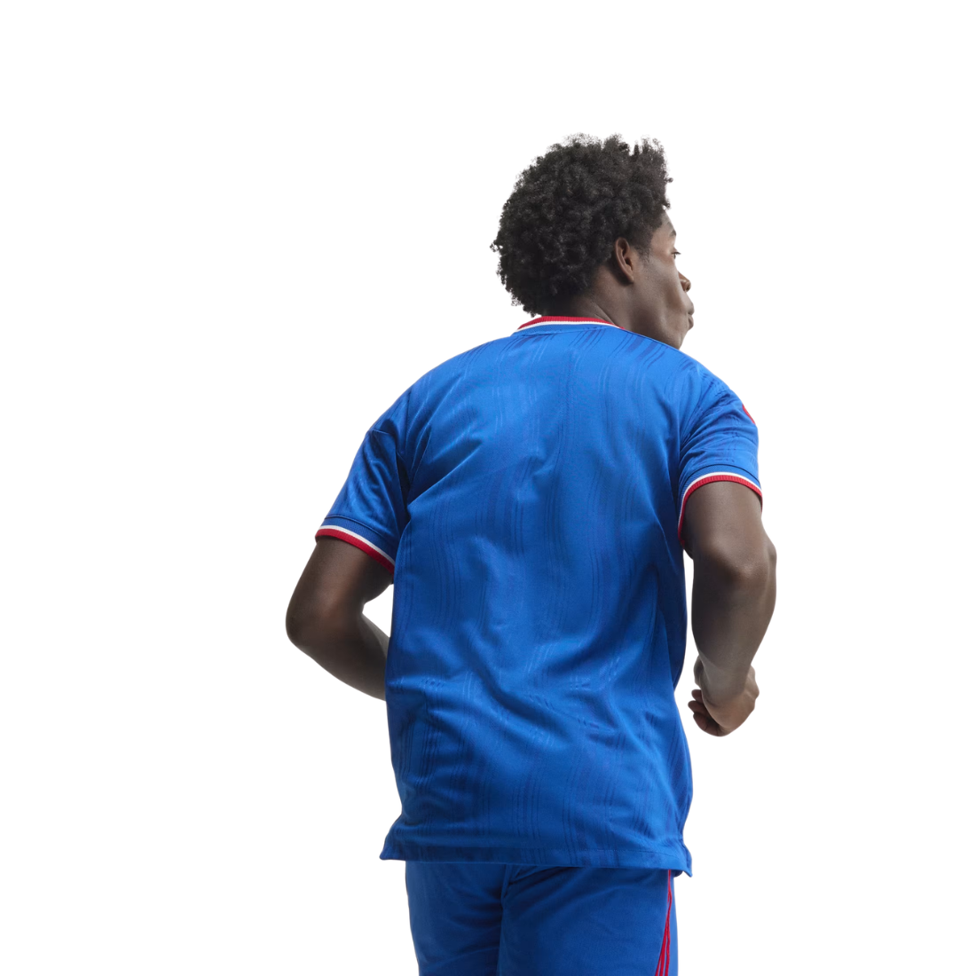 A man viewed from behind wearing a royal blue athletic jersey and matching shorts with red and white trim on the sleeves and side, isolated on a white background.
