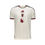 An Adidas Manchester United home soccer jersey in off-white with dark red and black accents, featuring the club's crest and Adidas logo on the front.