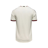 A short-sleeve athletic jersey shown from the back, featuring a cream-colored body with dark red trim on the sleeve cuffs and shoulder yokes, and thin black stripes along the upper shoulders.
