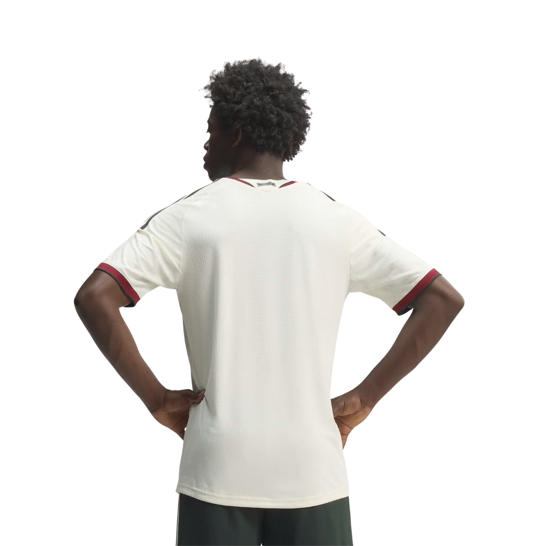 A man viewed from behind wearing a white short-sleeve athletic jersey with red trim on the sleeve cuffs and collar, paired with dark green shorts, against a plain white background.