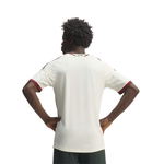 A man viewed from behind wearing a white short-sleeve athletic jersey with red trim on the sleeve cuffs and collar, paired with dark green shorts, against a plain white background.