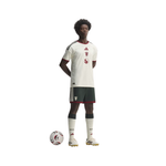 A full-body model wearing a white Adidas soccer jersey with dark green and red trim, matching dark green shorts, white socks, and white soccer cleats, standing next to a soccer ball on a plain white background.