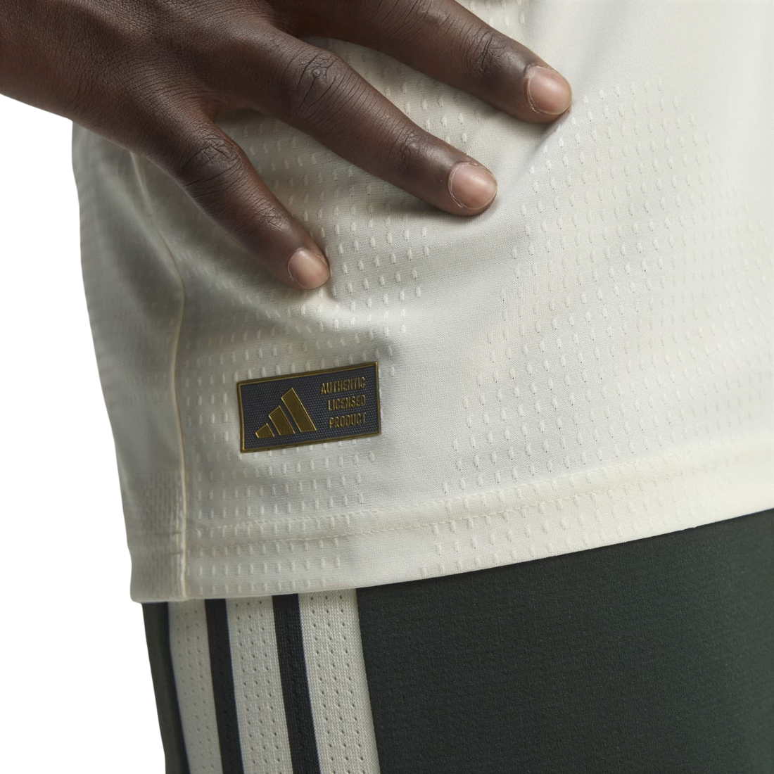 Close-up of a person wearing an Adidas jersey, showing the Adidas Performance patch on the side of the white textured fabric and part of the dark shorts.