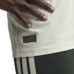 Close-up of a person wearing an Adidas jersey, showing the Adidas Performance patch on the side of the white textured fabric and part of the dark shorts.