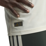 Close-up of a person wearing an Adidas jersey, showing the Adidas Performance patch on the side of the white textured fabric and part of the dark shorts.